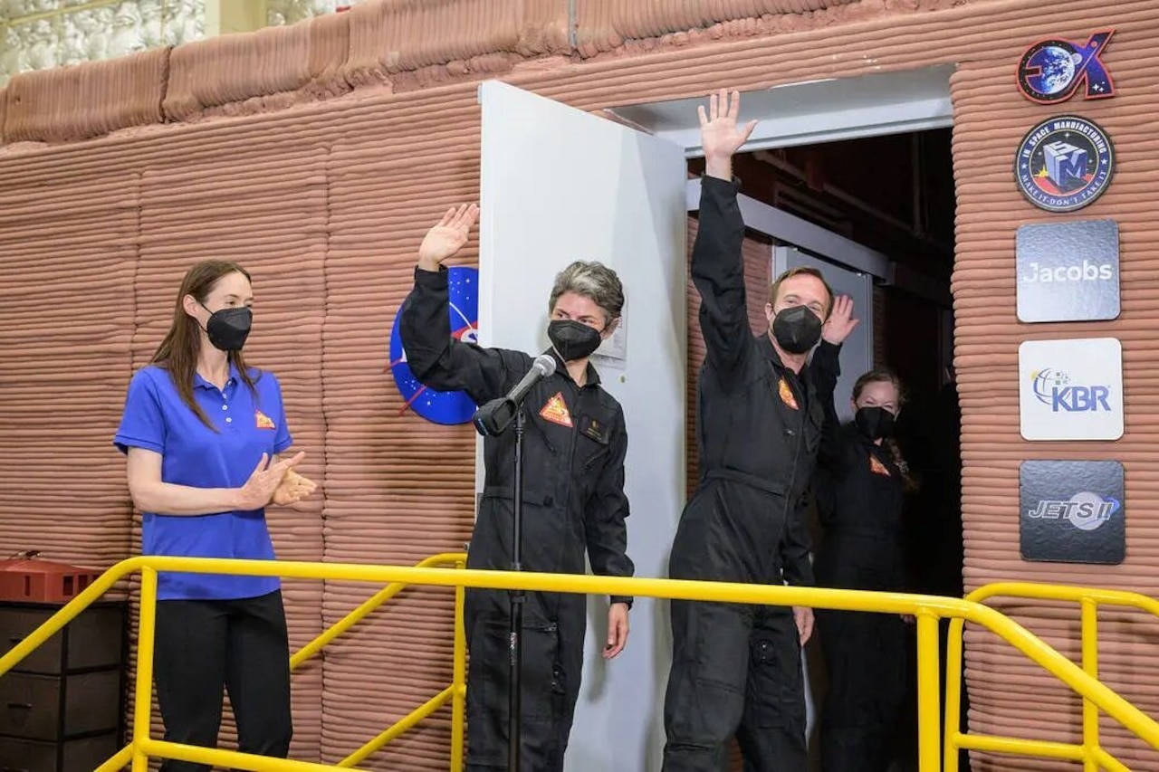 Three people wave to others as they walk into a building. A fourth person near them applauds.