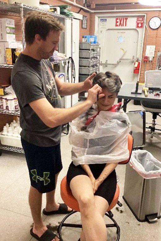 A woman sits in a chair while a man cuts her hair.