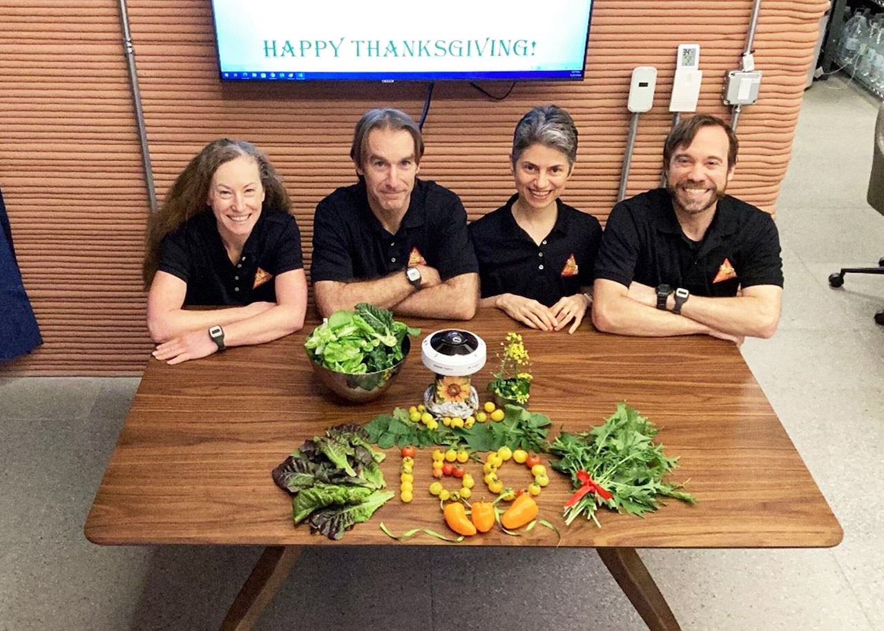 Four people sit at a table with vegetables on it.