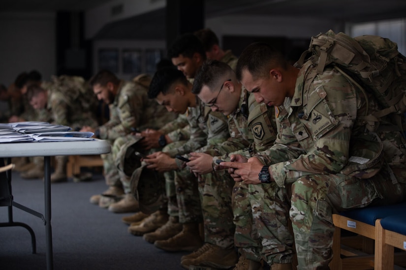 Dozens of soldiers bend while sitting on a bench.