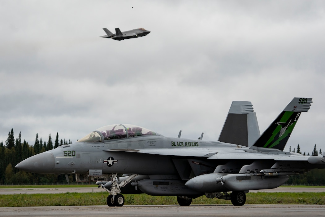 A U.S. Navy EA-18G Growler, assigned to the Electronic Attack Squadron 135 (VAQ-135) “Black Ravens”, taxis while a U.S. Air Force F-35 Lightning II, assigned to the 355th Fighter Squadron, takes off during Red Flag-Alaska 24-3