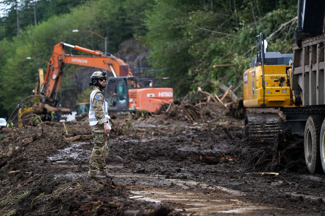 Alaska State Defense Force 2nd Lt. (AK) Matthew Nunnally, the acting Emergency Operations Center safety officer, directs heavy equipment operators while conducting debris clean up and recovery operations August 27, 2024, following a major landslide in Ketchikan, Alaska, two days earlier. Four Alaska Army National Guardsmen and two members of the Alaska State Defense Force mobilized on State Active Duty to assist with response efforts.