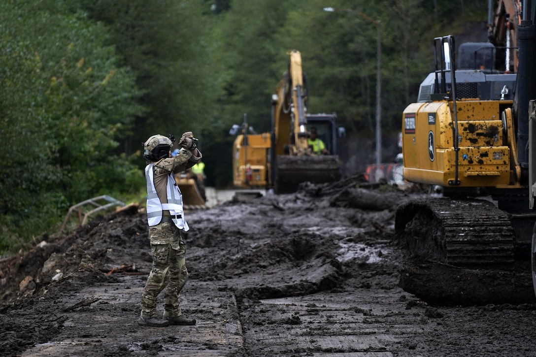 Alaska State Defense Force 2nd Lt. (AK) Matthew Nunnally, the acting Emergency Operations Center safety officer, directs heavy equipment operators while conducting debris clean up and recovery operations August 27, 2024, following a major landslide in Ketchikan, Alaska, two days earlier. Four Alaska Army National Guardsmen and two members of the Alaska State Defense Force mobilized on State Active Duty to assist with response efforts.