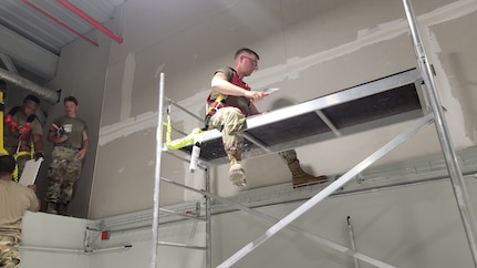 Airman sitting on scaffolding working on drywall