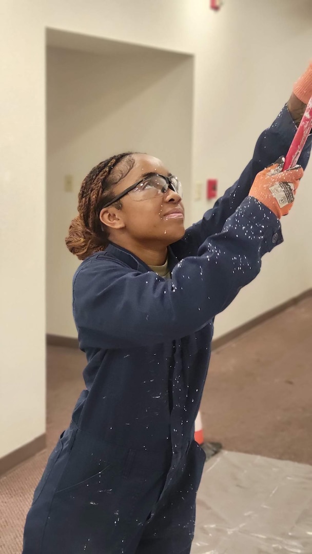 Airman painting a wall in a blue jumpsuit