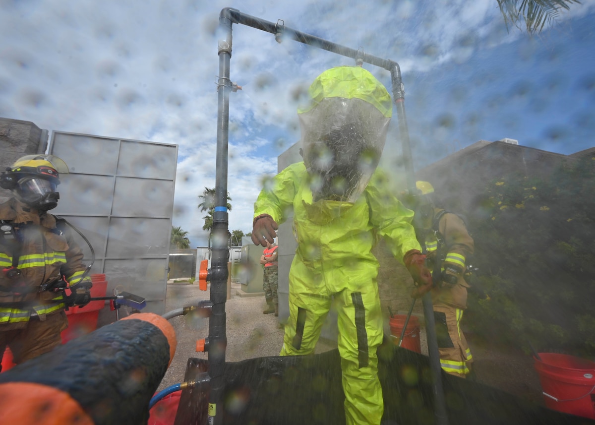 A man in a hazmat suit is scrubbed down by firefighters