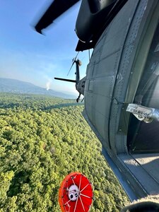 A Tennessee National Guard UH-60 Black Hawk helicopter from Knoxville’s 1-230th Assault Helicopter Battalion flies to a river to pick up water with a bucket suspended under the aircraft. The water was used to fight wildfires in the Great Smoky Mountains National Park Aug. 27, 2024.