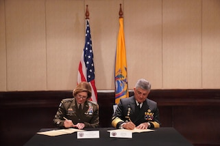 Military personnel sit at a table and sign documents.