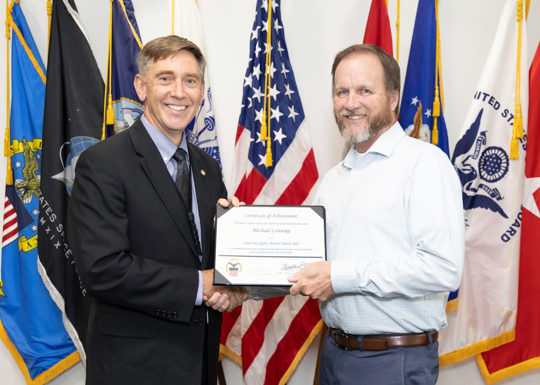 A man in a suit hands a certificate to a man in a white dress shirt.