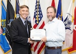 A man in a suit hands a certificate to a man in a white dress shirt.