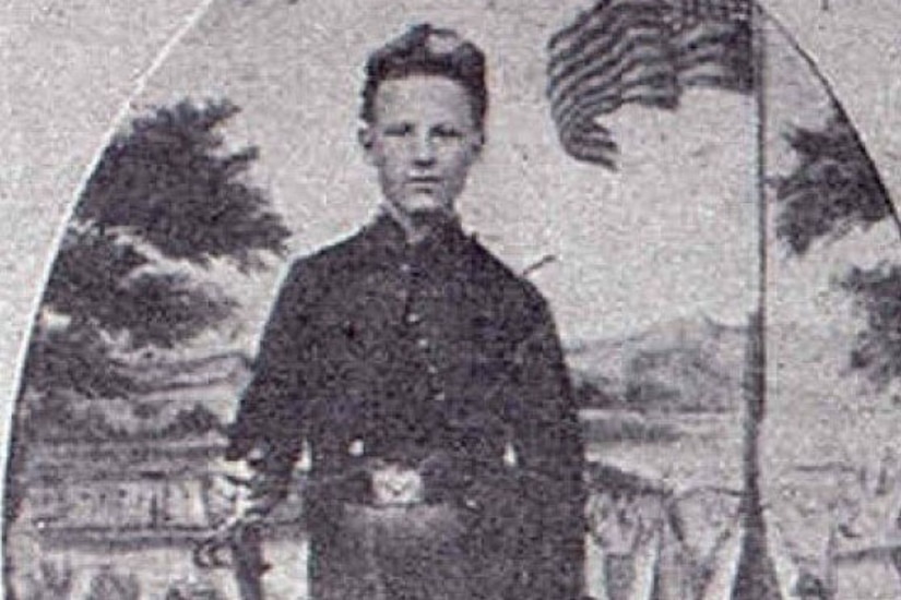 An old photograph shows a young boy holding a bugle beside an American flag.