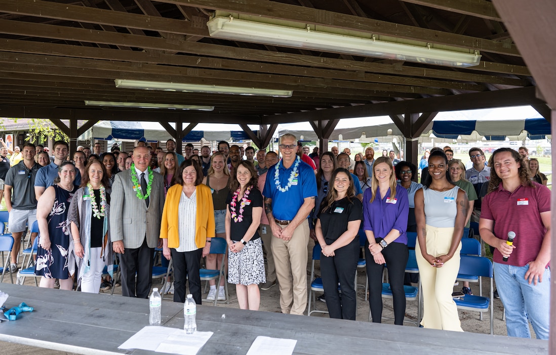 Leadership, event planners and attendees pose for a group photo under a canopy.