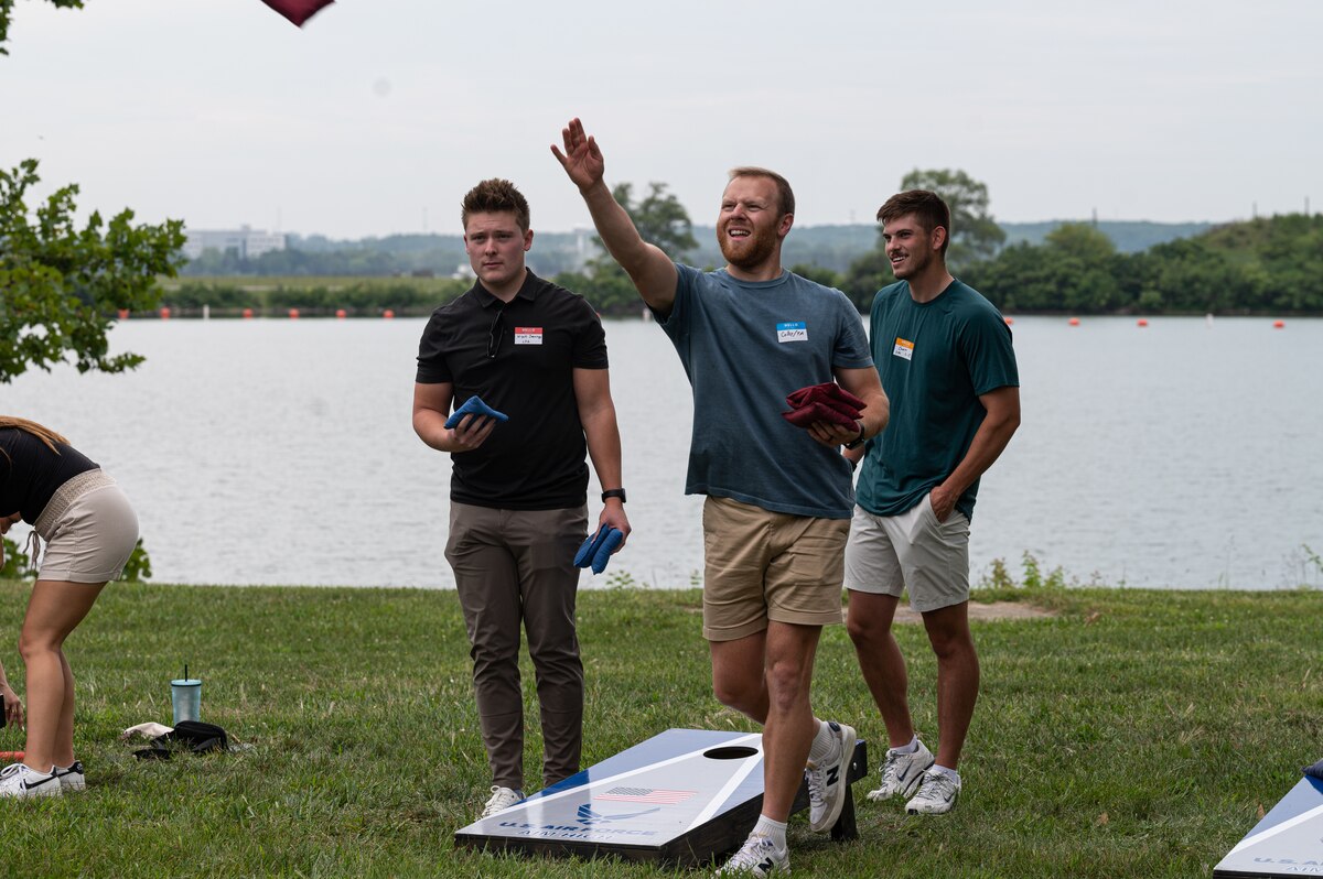 Attendees participate on a corn hole tournament by a body of water.