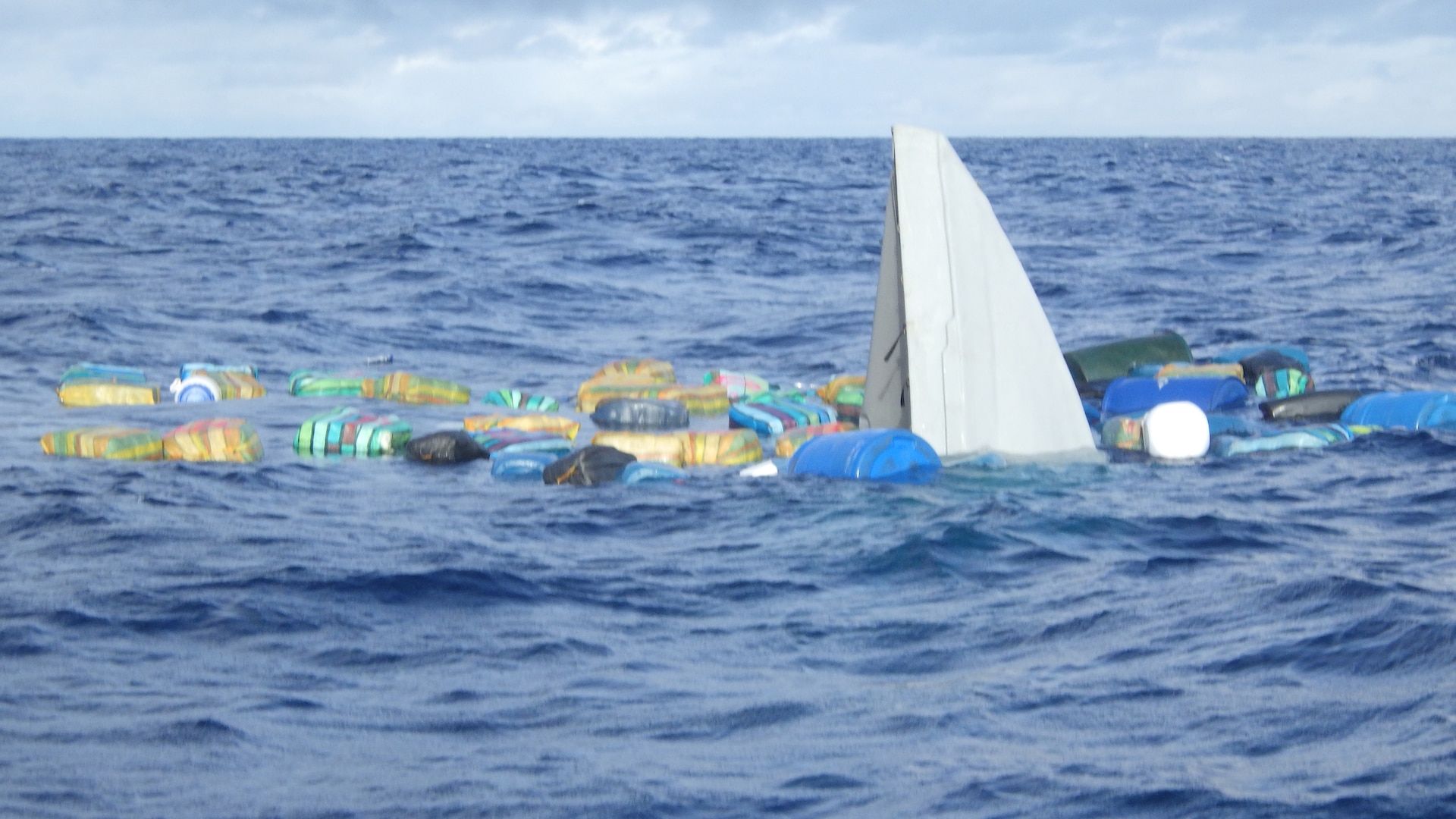 An image of a partially submerged go-fast vessel with bales of contraband containing illicit narcotics and fuel barrels floating in the Eastern Pacific Ocean, Aug. 3, 2024. The crew of U.S. Coast Guard Cutter Escanaba (WMEC 907) offloaded more than 3,400 pounds of cocaine and 4,410 pounds of marijuana with a combined assessed street value of approximately $50 million in Port Everglades, Florida, Aug. 23, 2024. (U.S. Coast Guard photo by Petty Officer 2nd Class Samuel Handy)