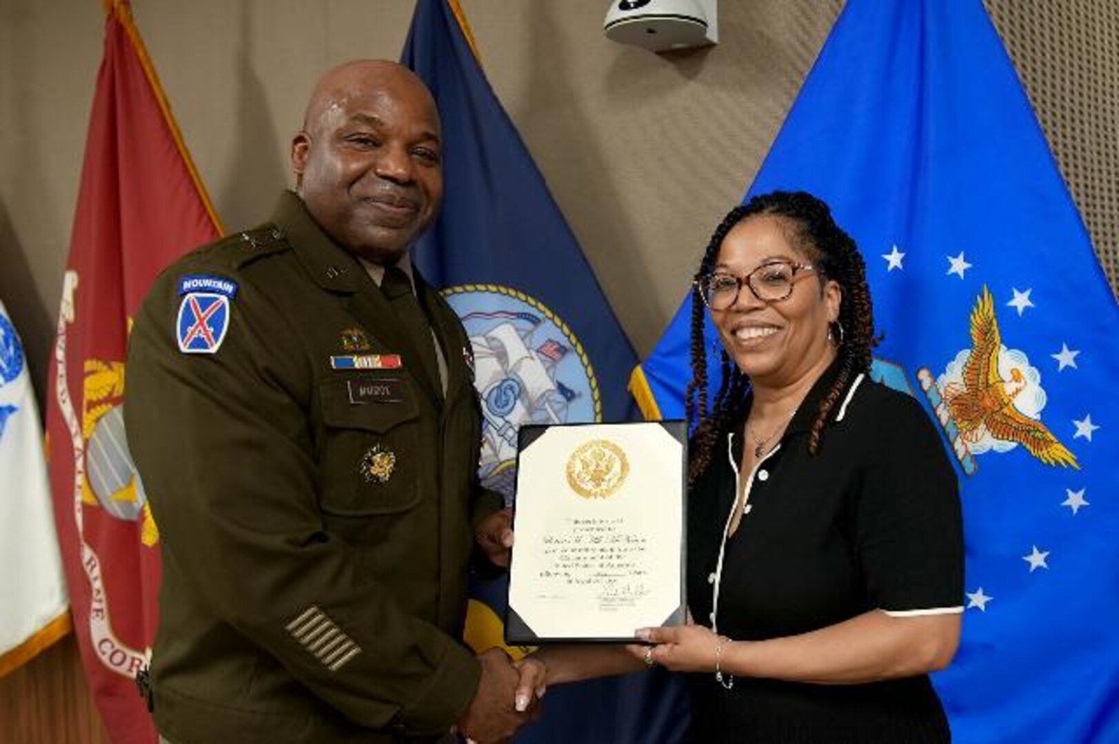 Army general and woman shake hands and hold certificate