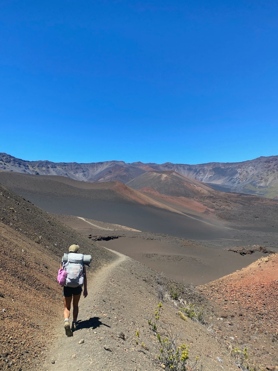 A person wearing a backpack and hat walks on a deserted dirt path.