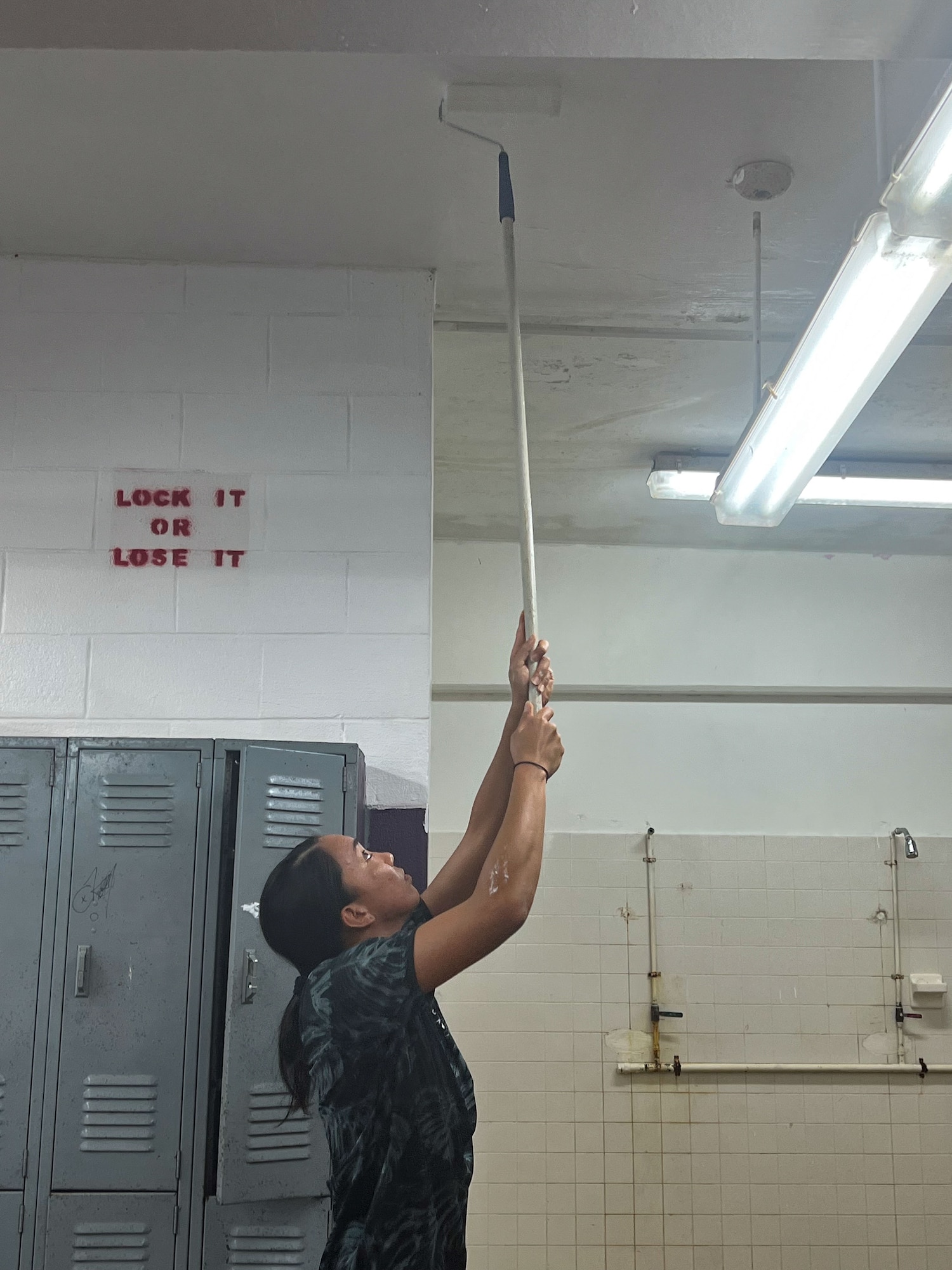 A U.S. Air Force female Airman from the 36th Force Support Squadron paints the ceiling by using a paint roller.