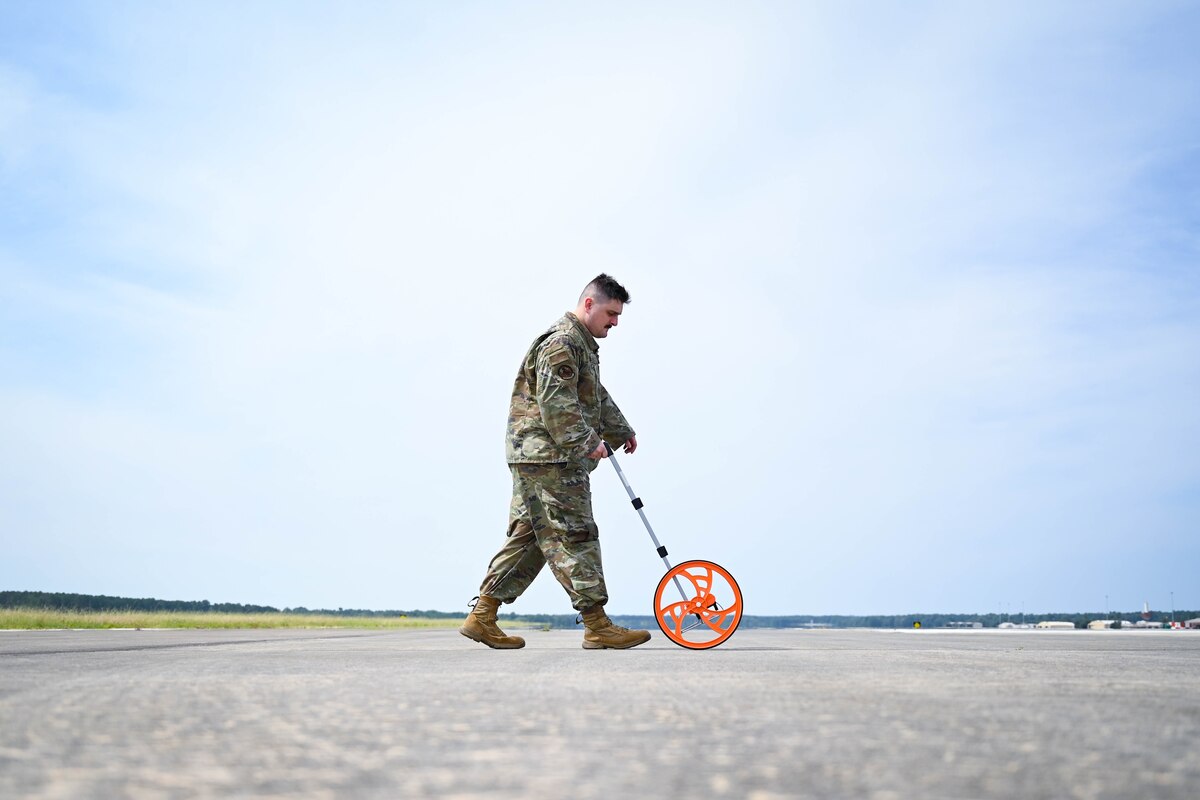 An Airman uses a measuring wheel to measure the flightline.