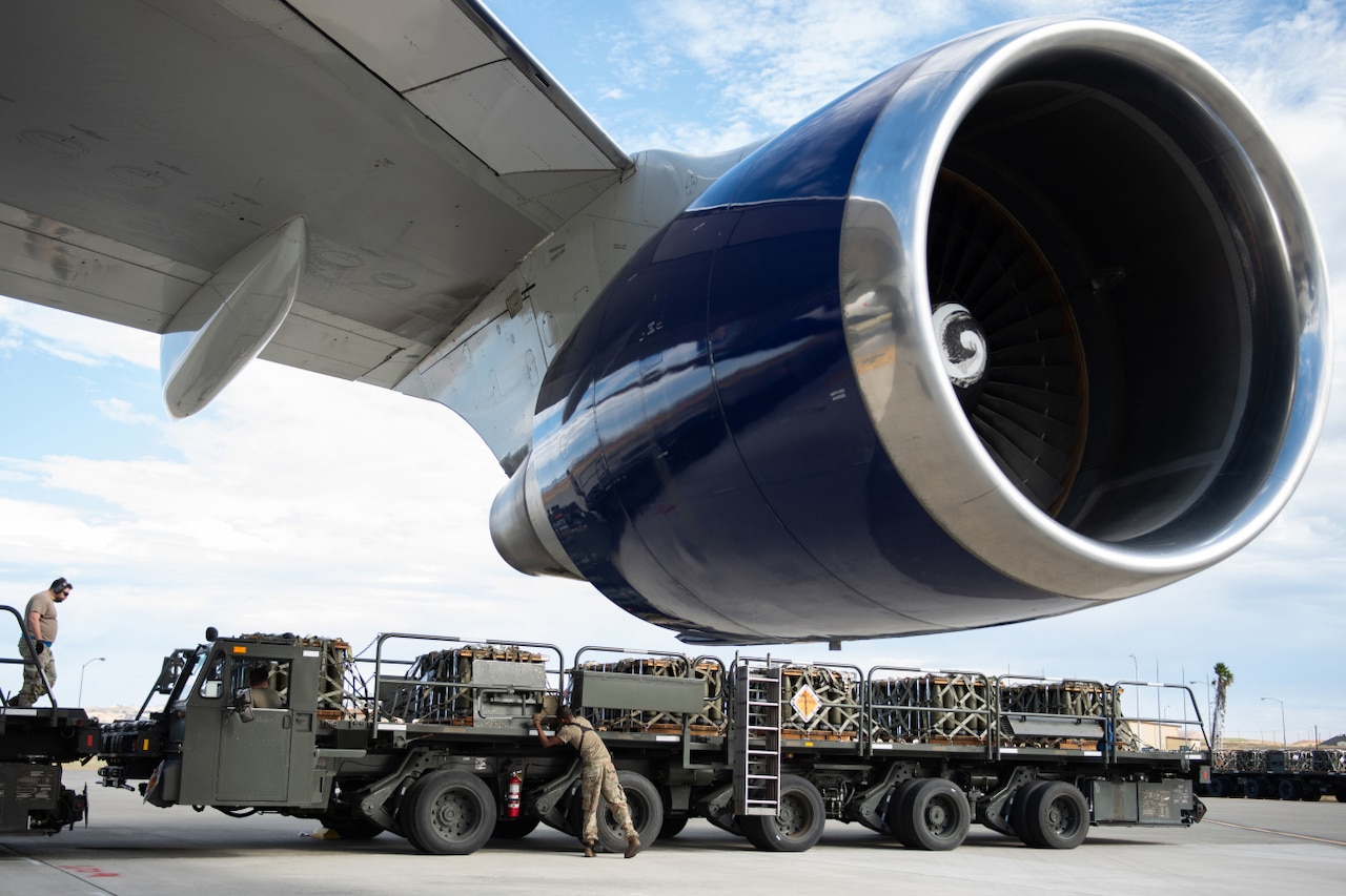 Service members load pallets of weapons onto an aircraft.