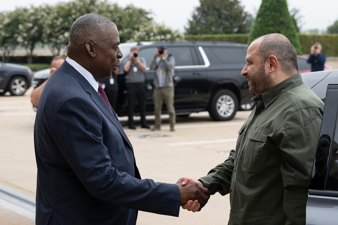 Two people shake hands as photographers snap photos.