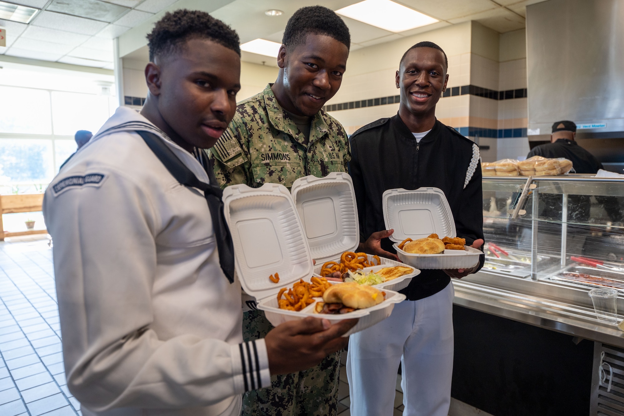 sailors stand in dining hall holding takeout food