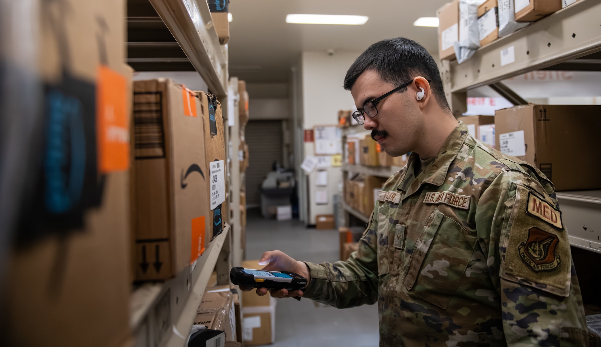 An Airman stands in the middle of an aisle scanning boxes at a post office.