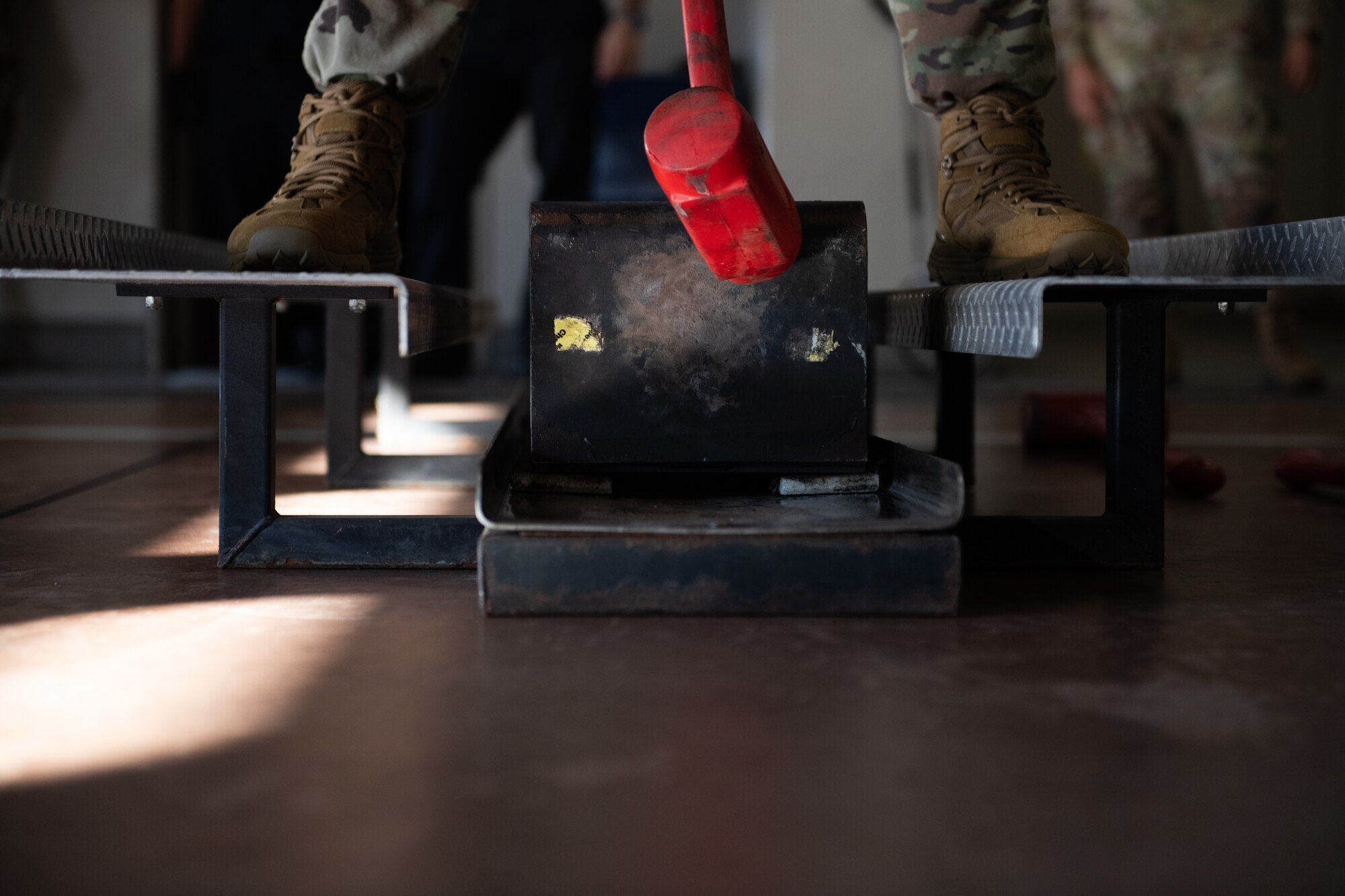 An Airmen swings a red mallet at a weight.