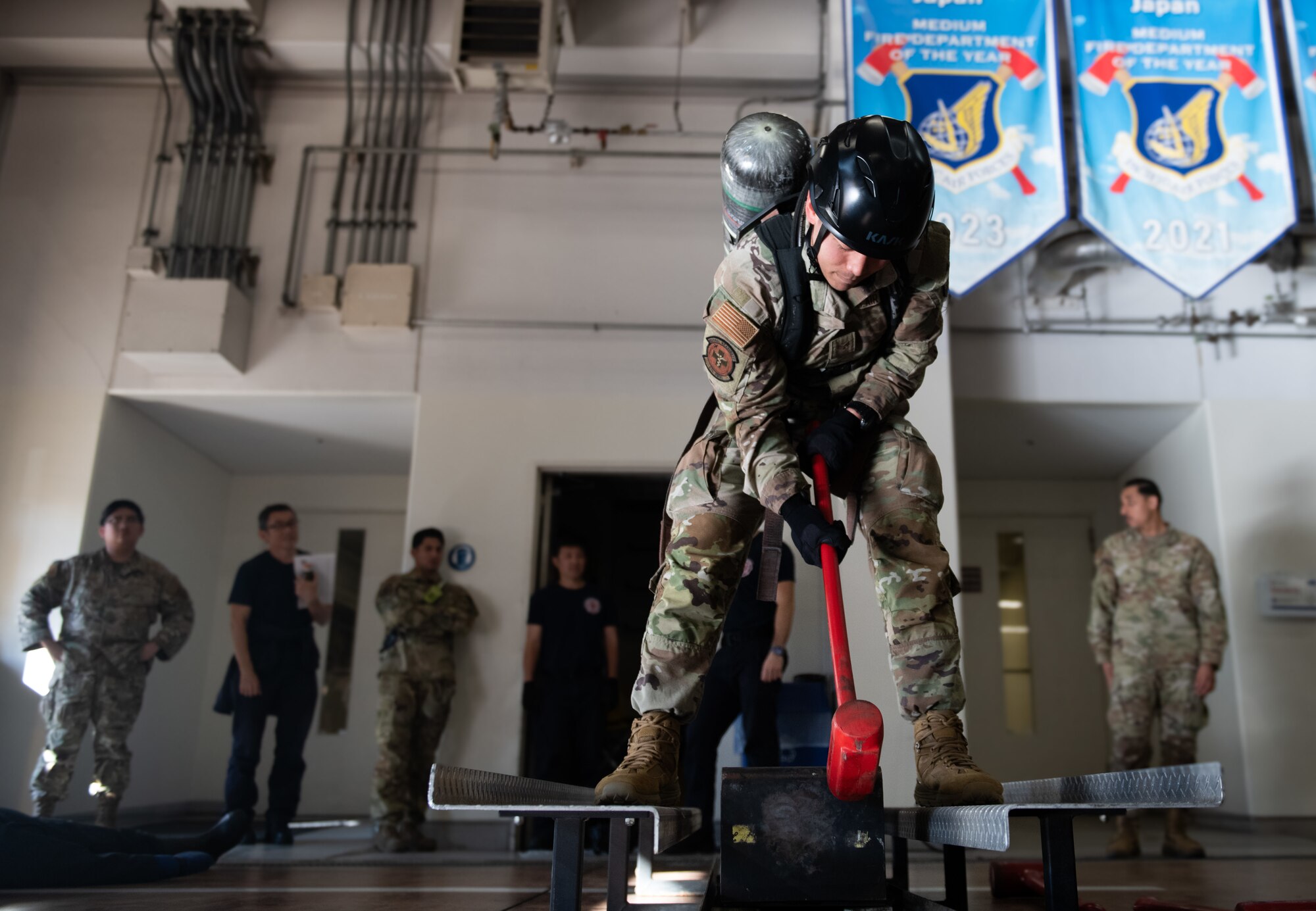 An Airmen swings a red mallet at a weigh while wearing fire fighter protective gear.
