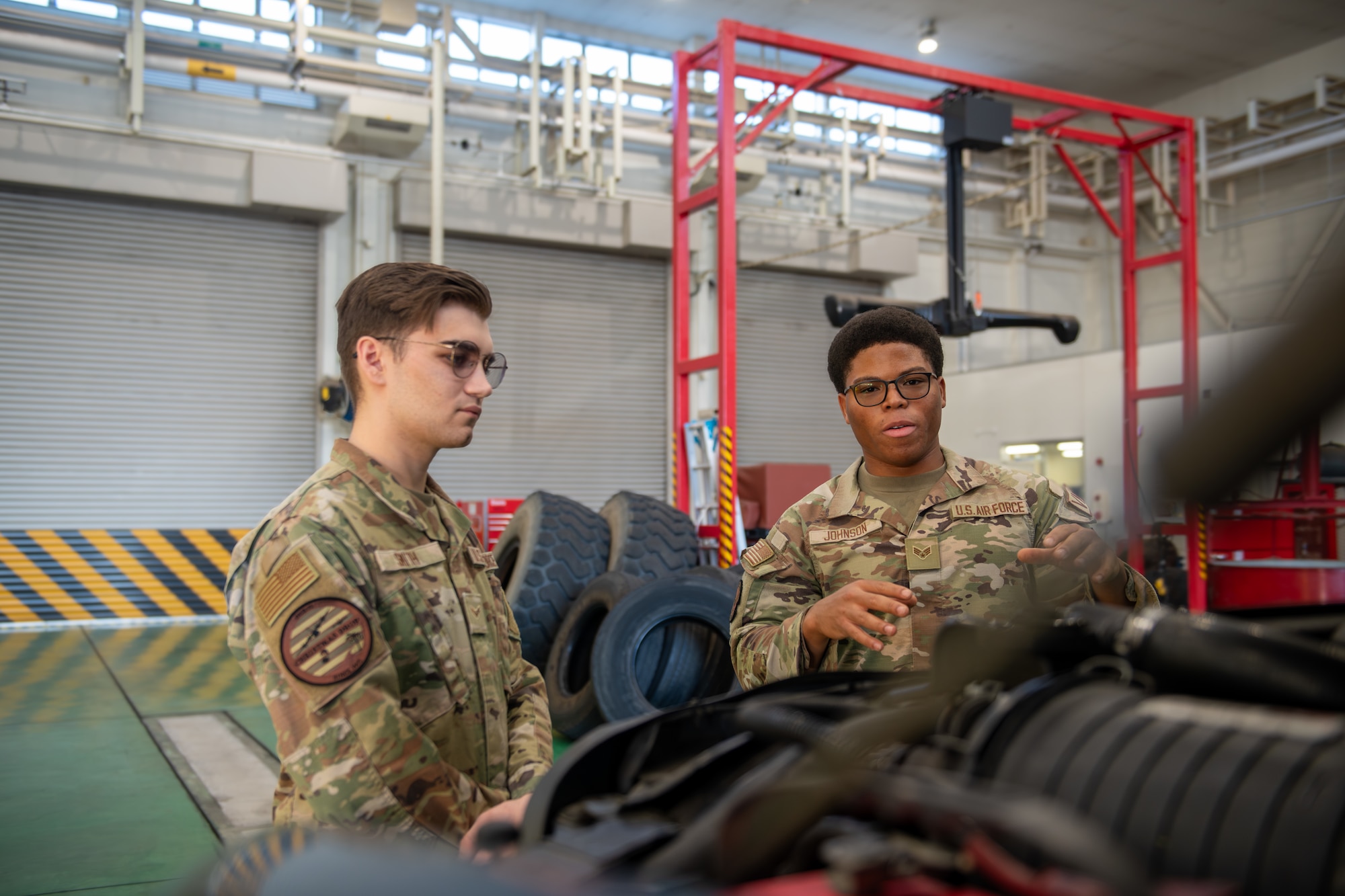 Two Airmen stand in front of a motor and discuss specifications.