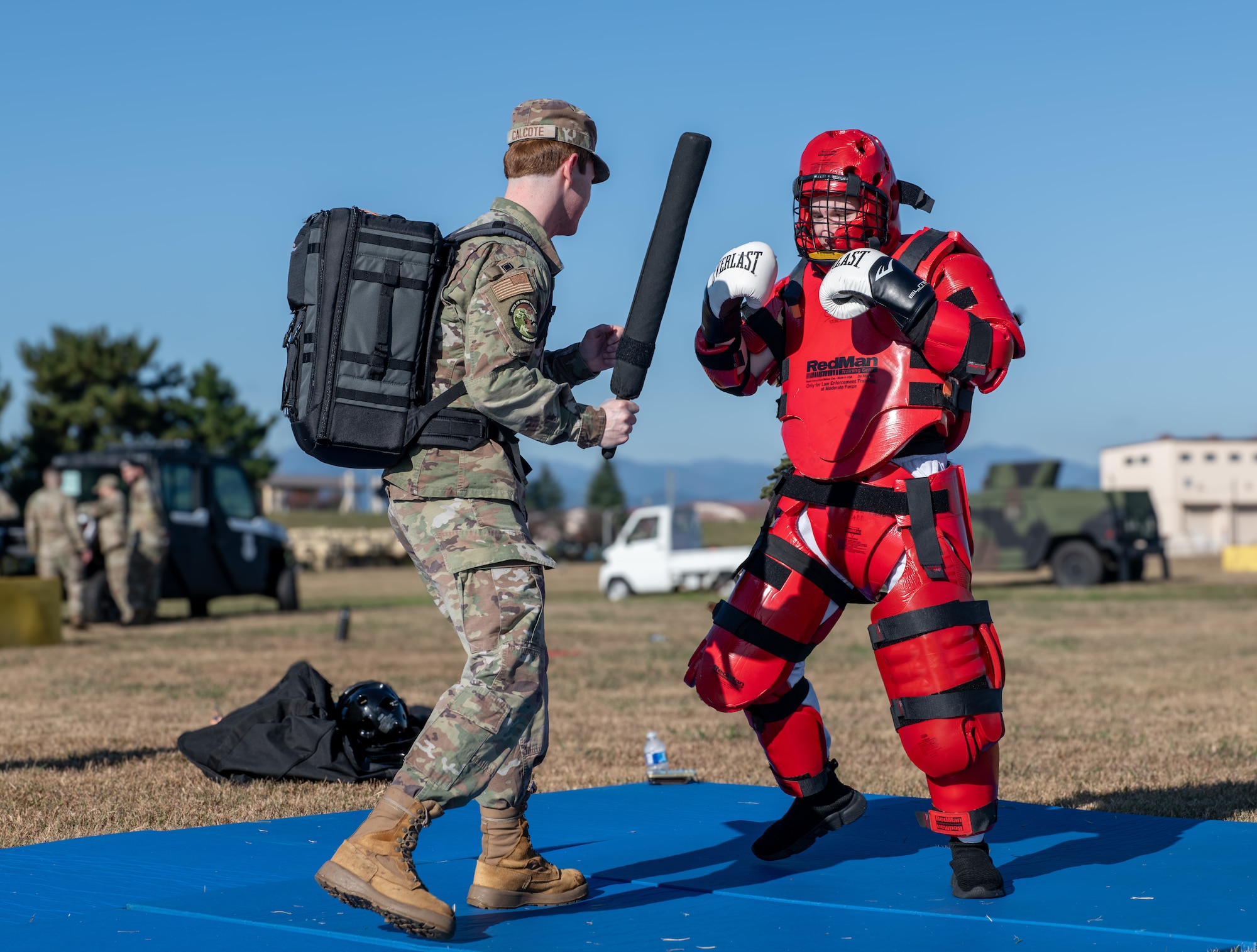 An airman engages in simulated baton combat against a guy in a red protective suit.