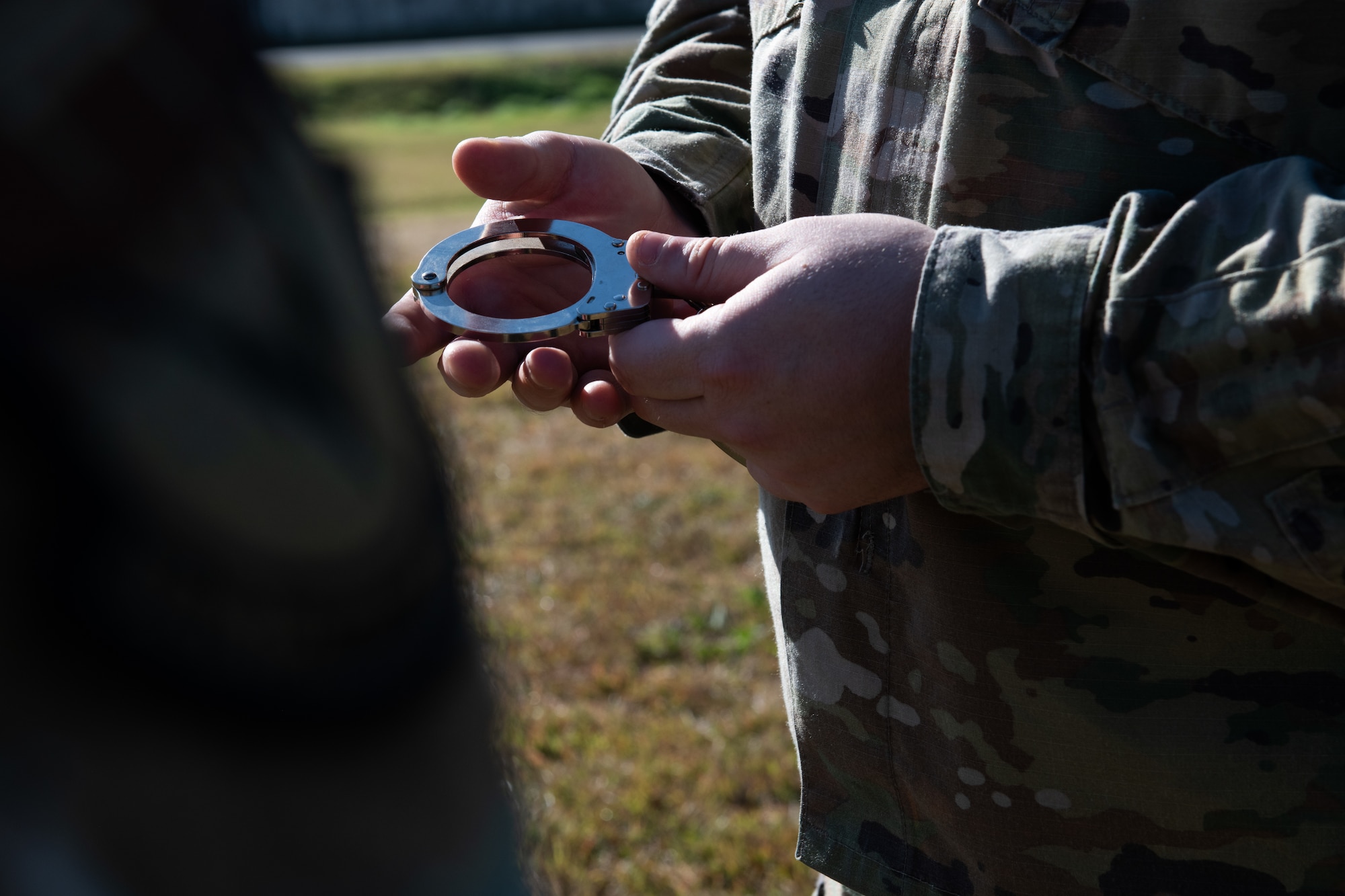 An airmen holds silver handcuffs in their hands.