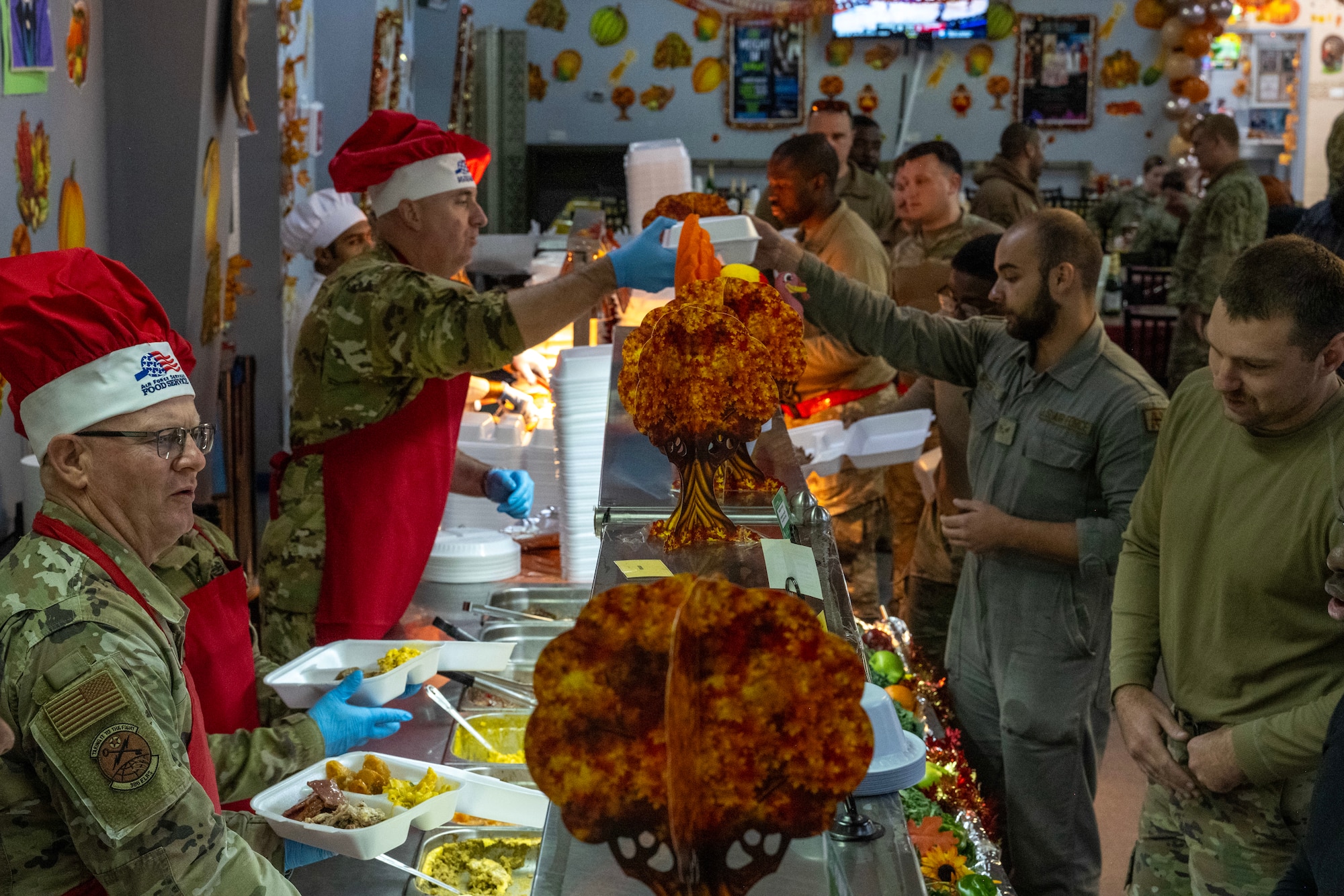 Leadership serves a Thanksgiving meal as service members go through a line at a dining facility.
