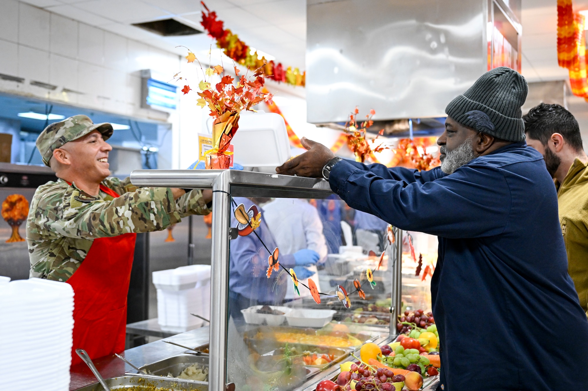 A first sergeant wearing a red apron serves a plate of food during a Thanksgiving meal at the dining facility.