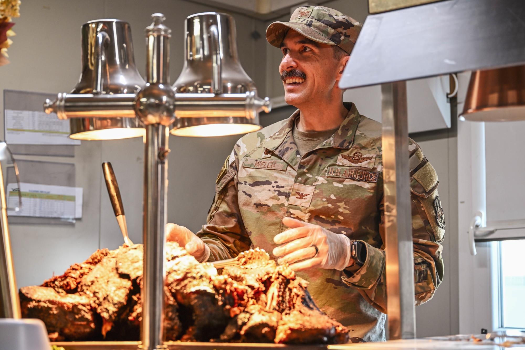 A commander works at a carving station during a Thanksgiving meal in the dining facility.