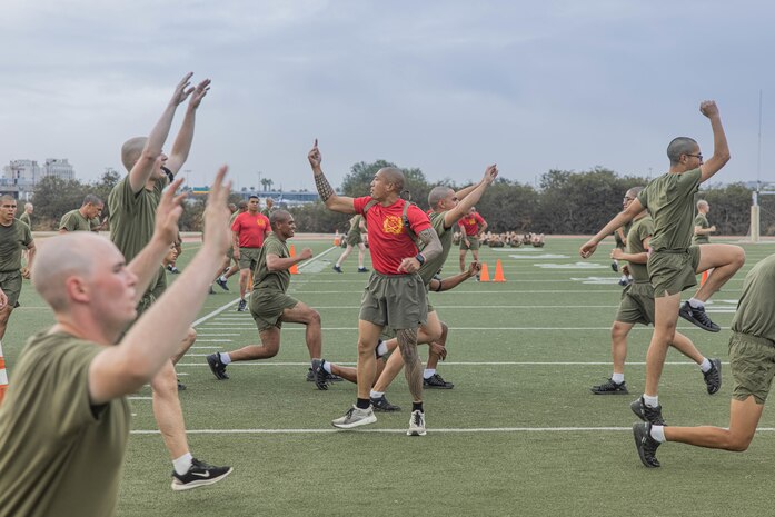 U.S. Marine Corps Drill Instructor Sgt. Bronson Sahut, center, with Bravo Company, 1st Recruit Training Battalion, observes recruits executing exercise during a physical training event at Marine Corps Recruit Depot San Diego, California, Nov. 27, 2024. The recruits conducted a series of stations such as side shuffles, ammunition can lifts, planks, single-leg Romanian deadlifts, bicycle crunches, and 440-yard sprints during their physical training event, strengthening themselves physically and mentally. (U.S. Marine Corps photo by Cpl. Alexandra M. Earl)