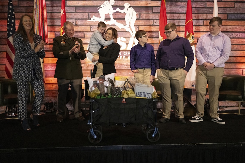 A group of adults, teens and kids stand on a stage, some applauding.