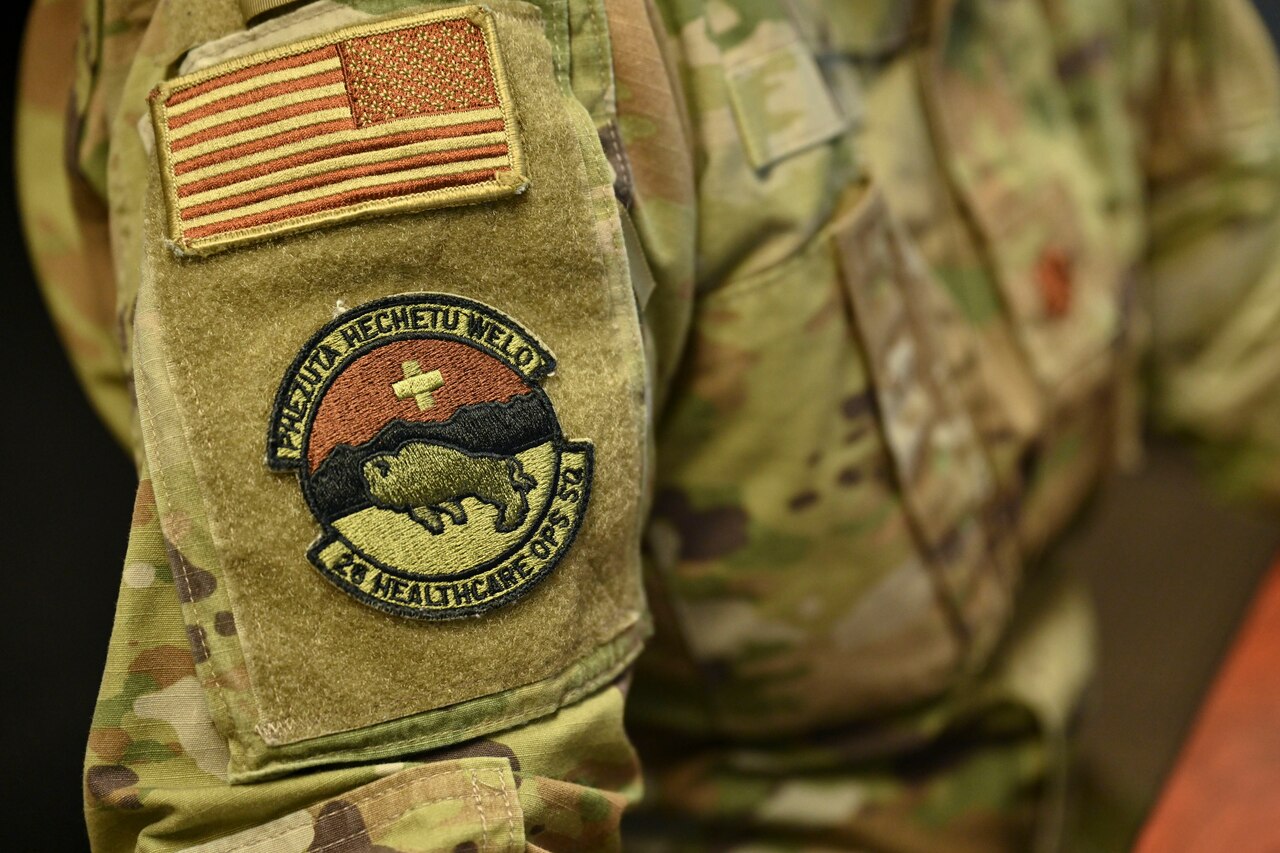 The torso and arm of an airman displaying a logo and the American flag on the shoulder pad of a military uniform.