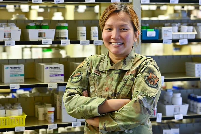 An airman smiles in front of shelves filled with medicine and prescription durgs.