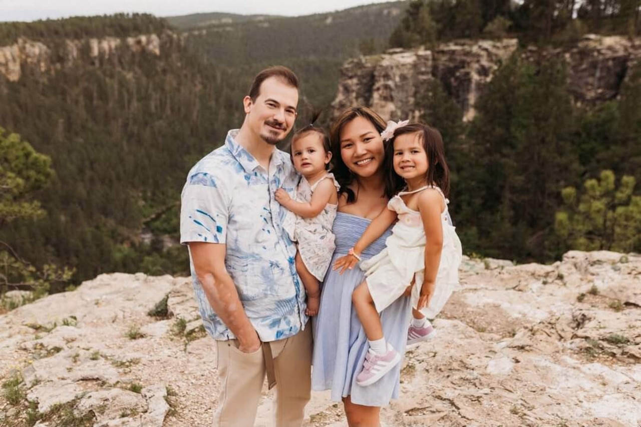 Two parents and two children pose for a photo in front of a canyon filled with trees.