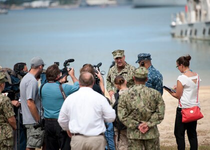 Officer is surrounded by media personnel while the water is in the background.