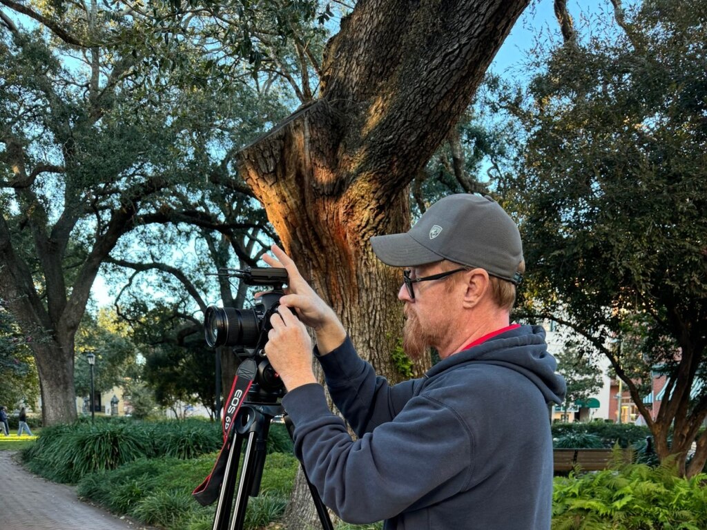 Male taking a picture with greenery in the background.