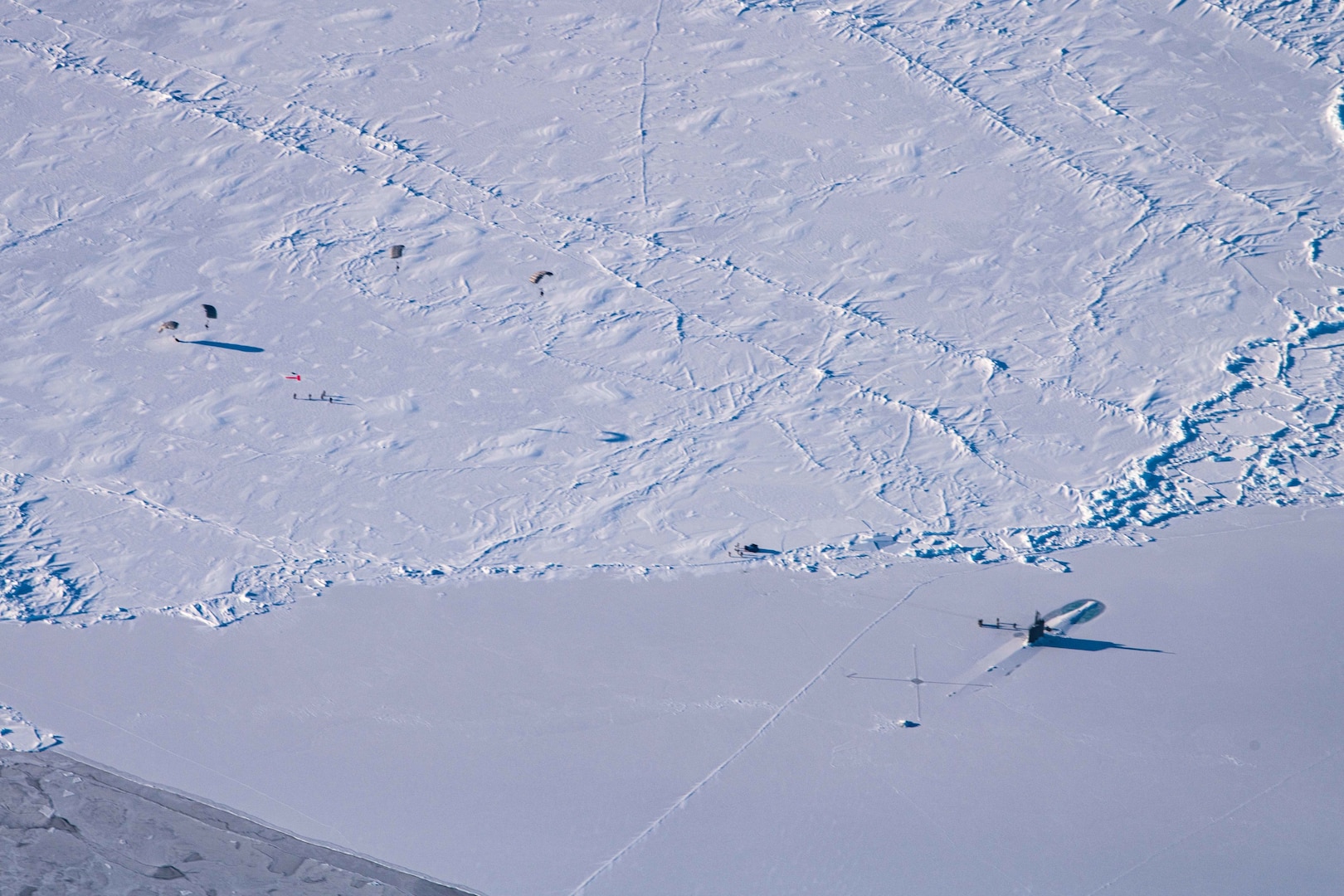 Submarine appearing through ice, parachuters landing on ice field