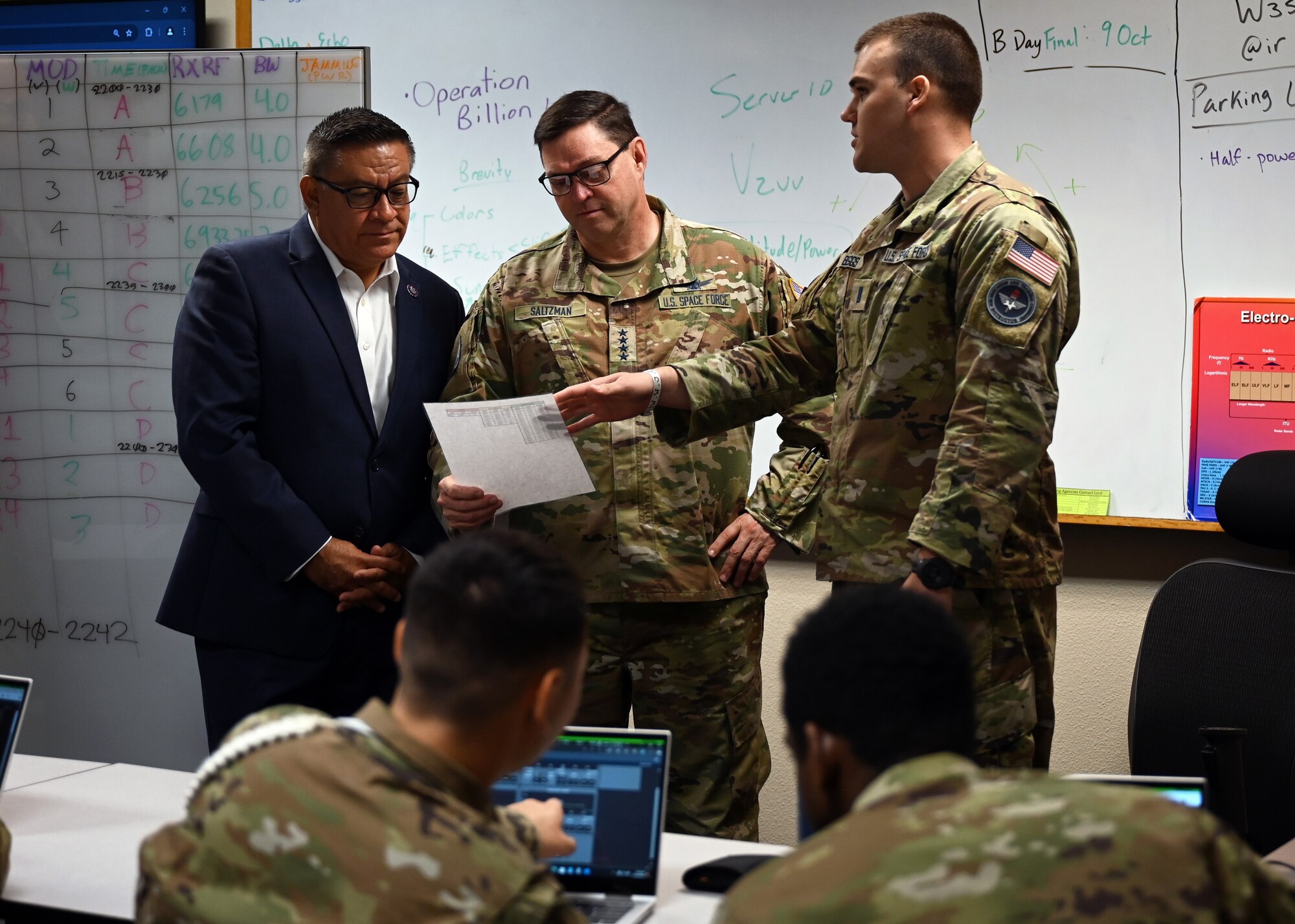 Three men stand in a classroom while they conversate over a paper.