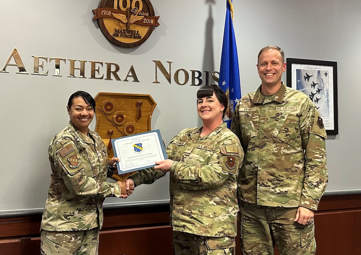 U.S. Air Force Staff Sgt. Alexandra Edwards, center, 42nd Medical Group Commander Support Staff NCOIC, receives the "Crusader of the Month" award from Col. Shamekia Toliver, left, 42nd Air Base Wing commander, and Chief Master Sgt. Caleb Vaden, right, 42nd ABW command chief, for her exceptional service and leadership at Maxwell Air Force Base, Ala., Nov. 30, 2024.