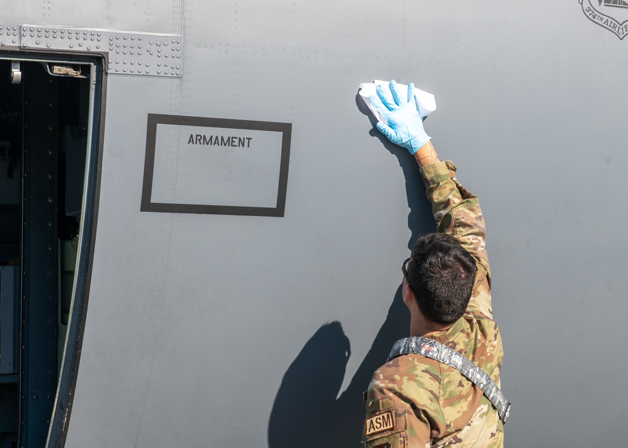 An Airman uses a cloth to wipe the side of a grey aircraft.