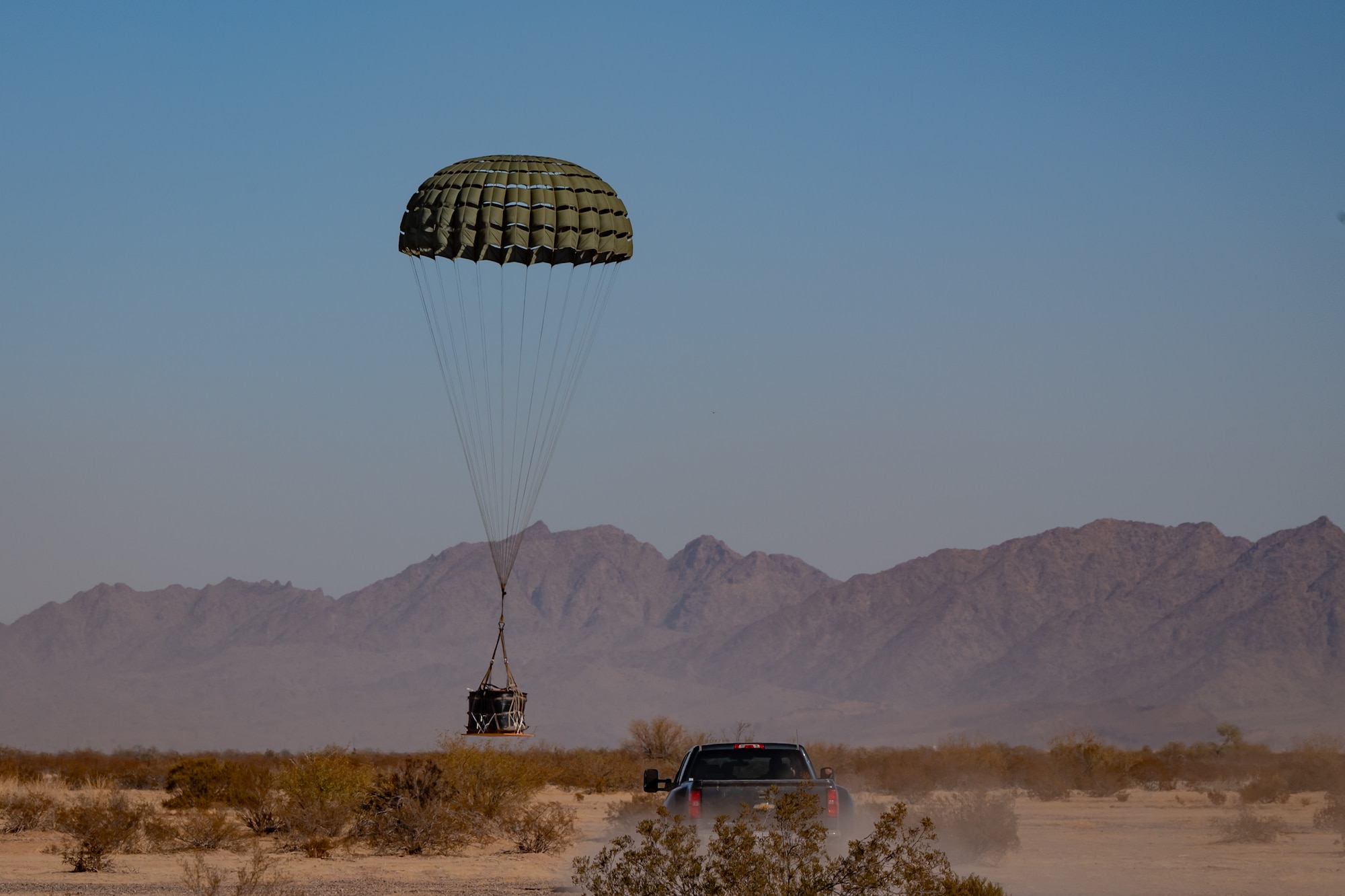 U.S. Air Force Airmen approach a cargo bundle safely descending from a U.S. Marine Corps KC-130J Hercules during an Exercise Desert Hammer 25-1 training mission at Auxiliary Airfield 6 near Gila Bend, Ariz., Nov. 14, 2024. Exercise Desert Hammer tests the operational readiness of over 700 participants across the Air Force Reserve, Air Force Active Duty, Arizona Army National Guard, and U.S. Marine Corps. (U.S. Air Force photo by Tech. Sgt. Tyler J. Bolken)