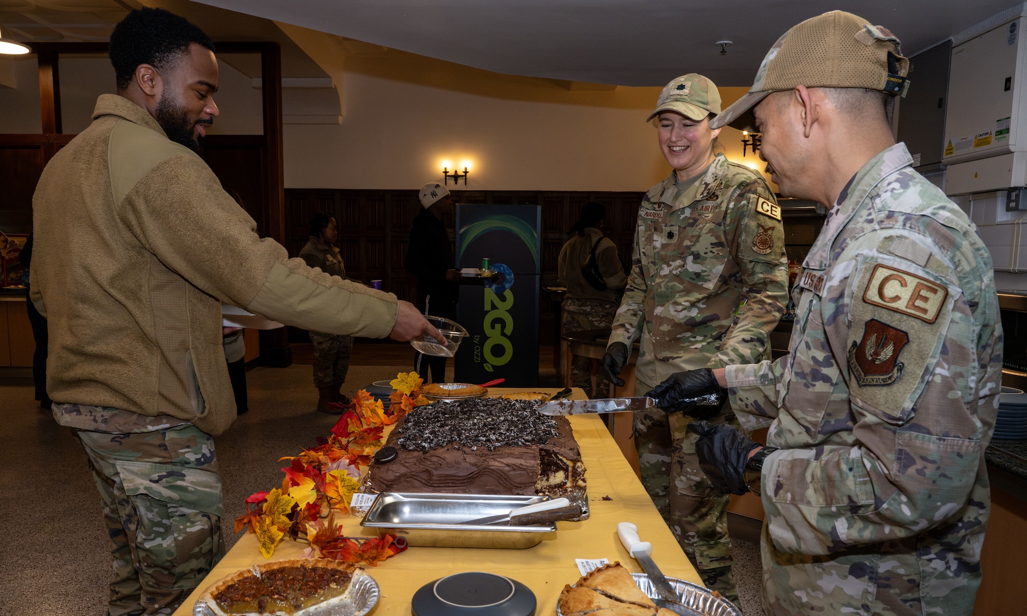 U.S. Air Force Lt. Col. Anna Narduzzi, center, 100th Civil Engineer Squadron commander, and Senior Master Sgt. Marlon Quitos, right, 100th CES senior enlisted leader, slice and distribute dessert to an Airman at Royal Air Force Mildenhall, England, Nov. 27, 2024.