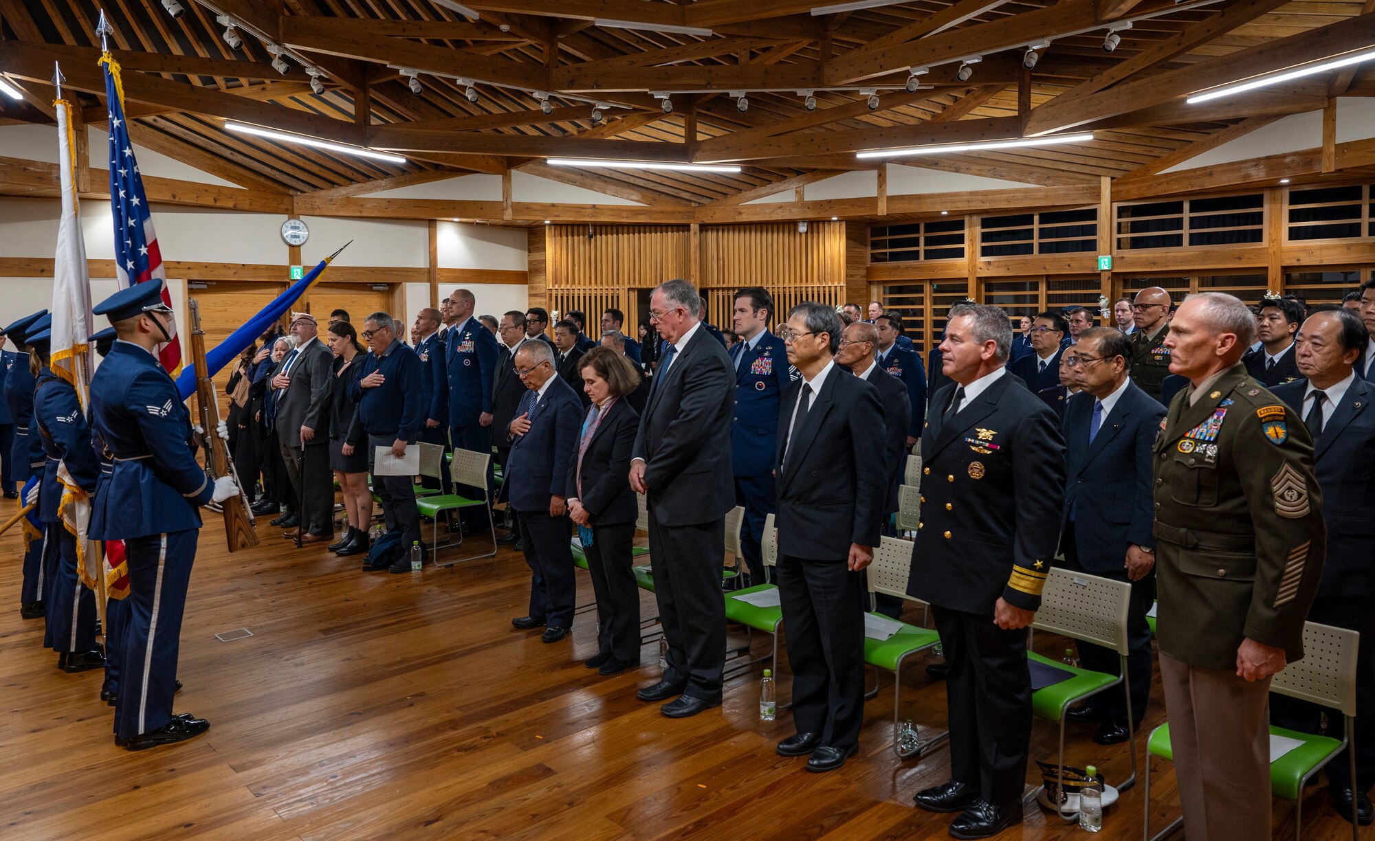 A group of people stand in a room facing four people holding flags.