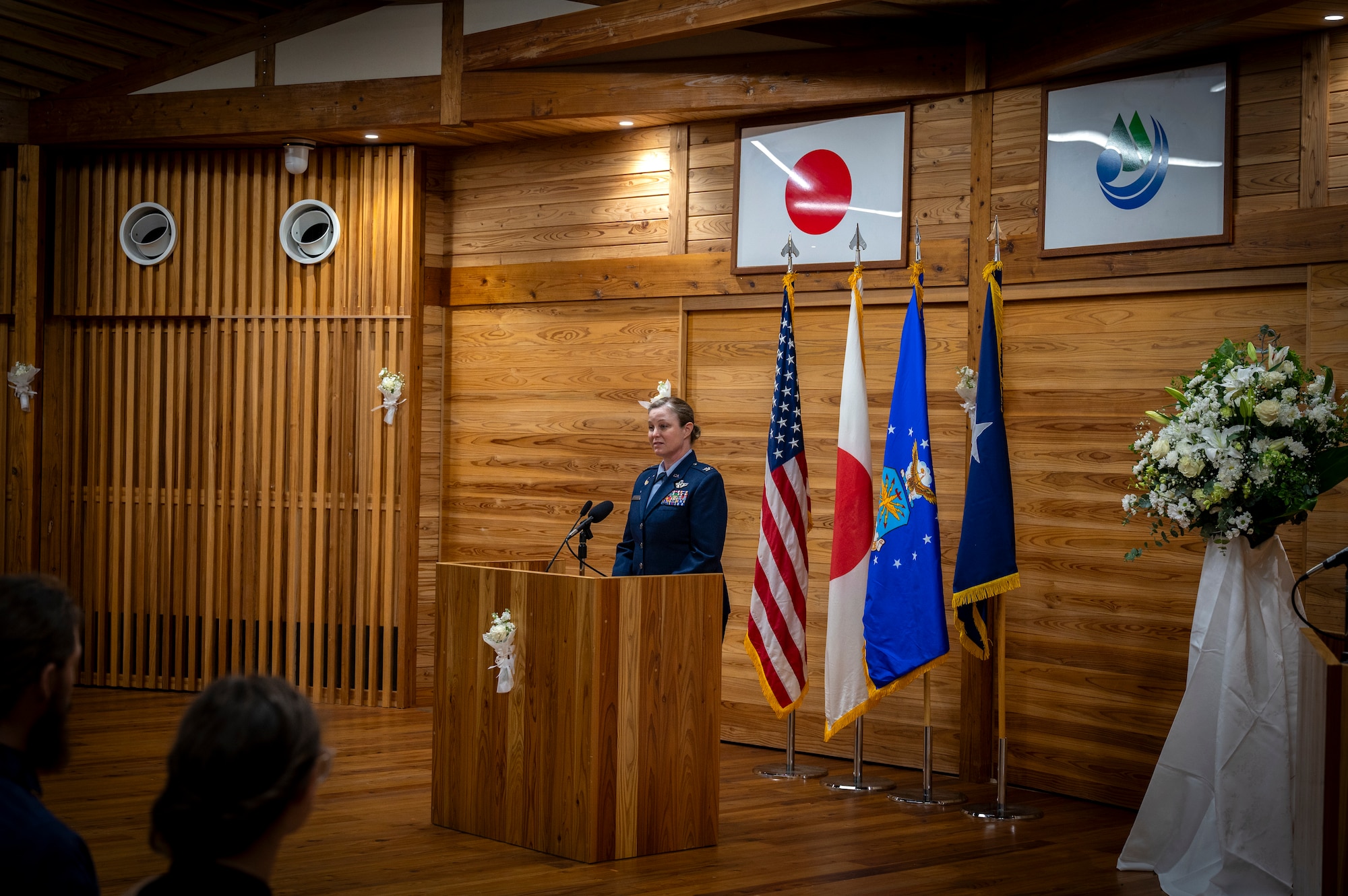 A woman stands behind a lectern and speaks into a microphone at the front of a room.