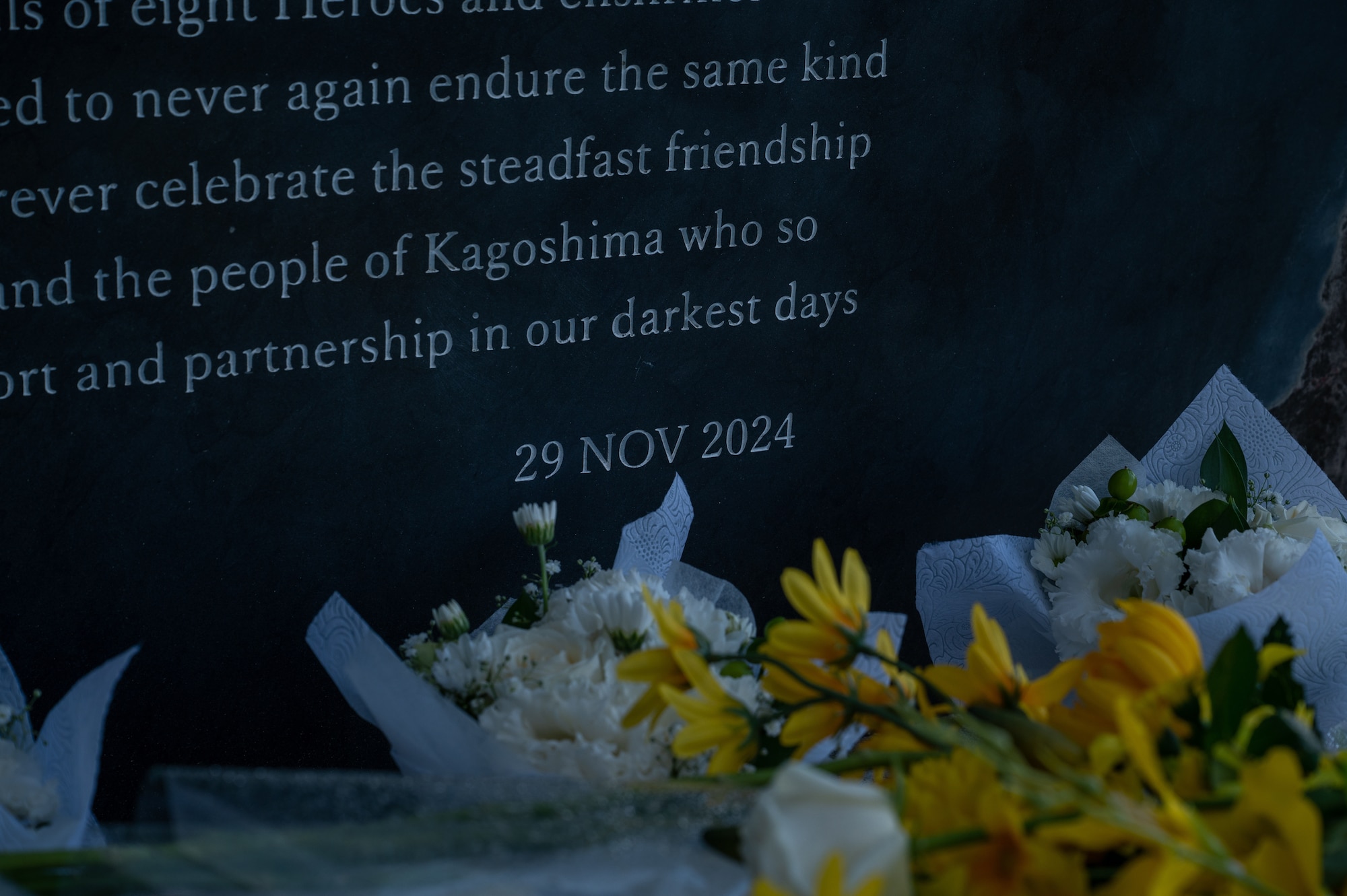 Flowers sit on concrete ledge in front of stone monument.